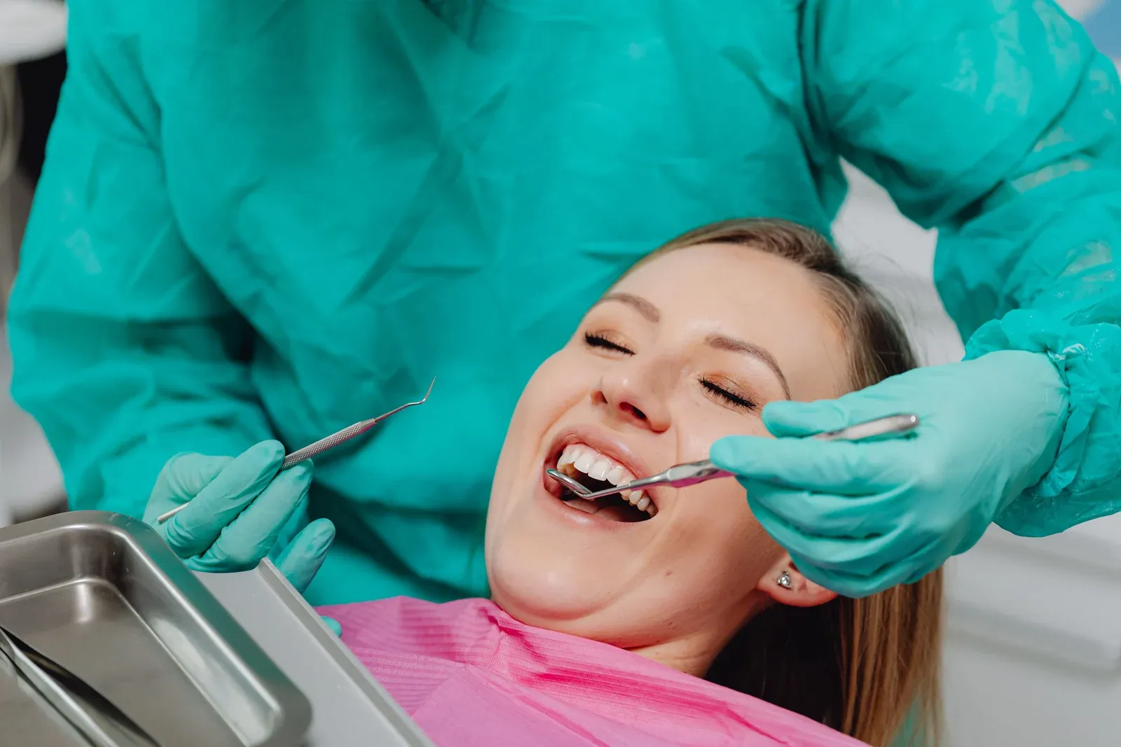 Mulher sorrindo durante uma avaliação odontológica com instrumentos de exame.