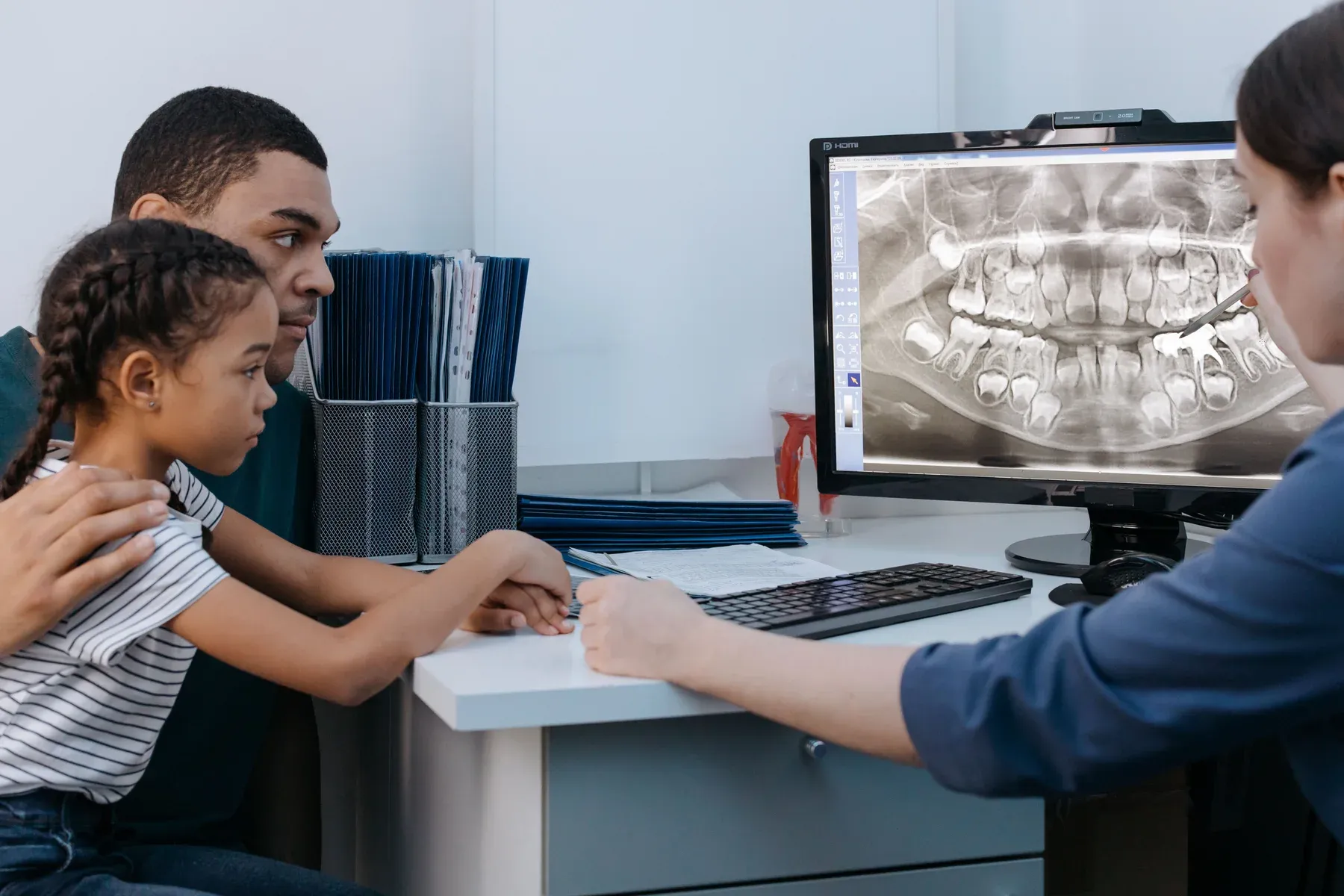 Criança acompanhada de um adulto durante uma conversa com dentista, diante de uma radiografia.